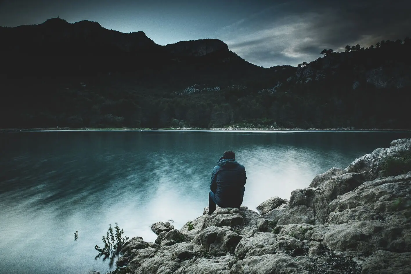 a man sitting on a rock looking at the water.