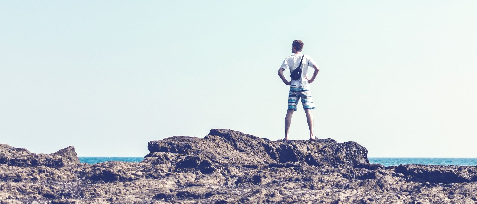 a man standing on top of a rock next to the ocean.