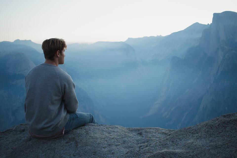 Young man in sweater sitting over edge of cliff admiring the scenic landscape