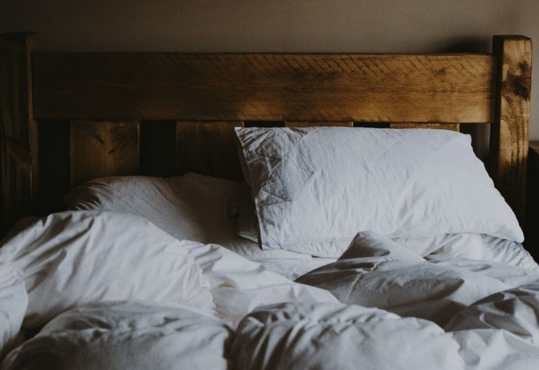 an unmade bed with white sheets and pillows.