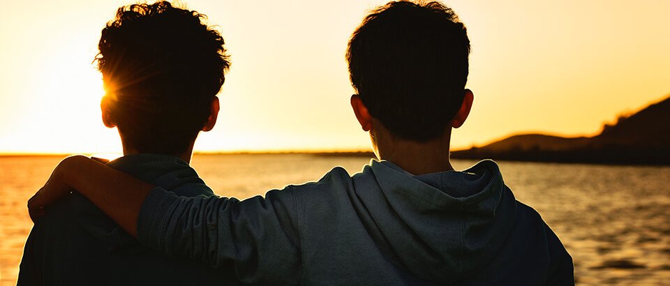 a couple of men standing next to each other near a body of water.