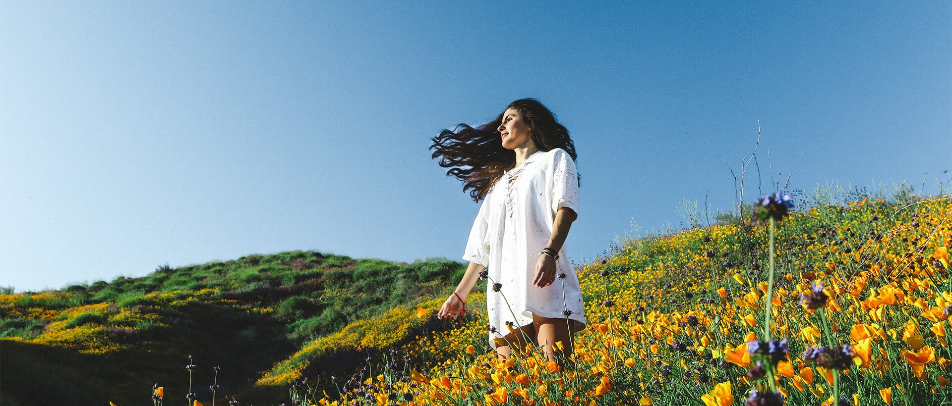 a woman walking through a field of flowers.