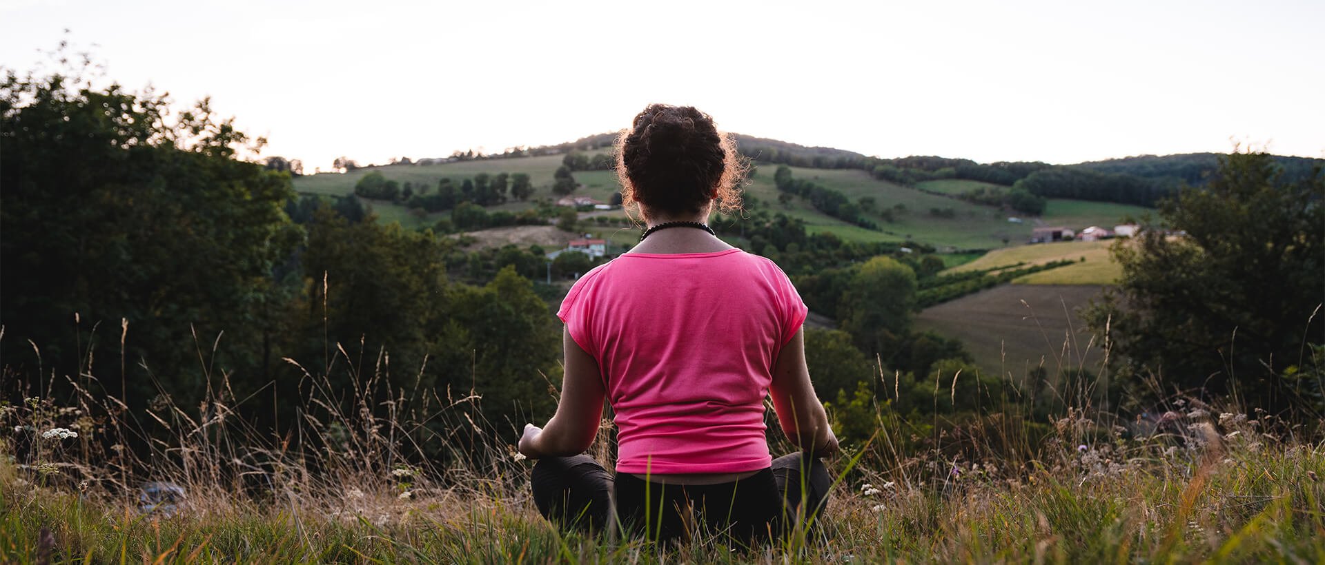 a woman in a pink shirt sitting in a field.