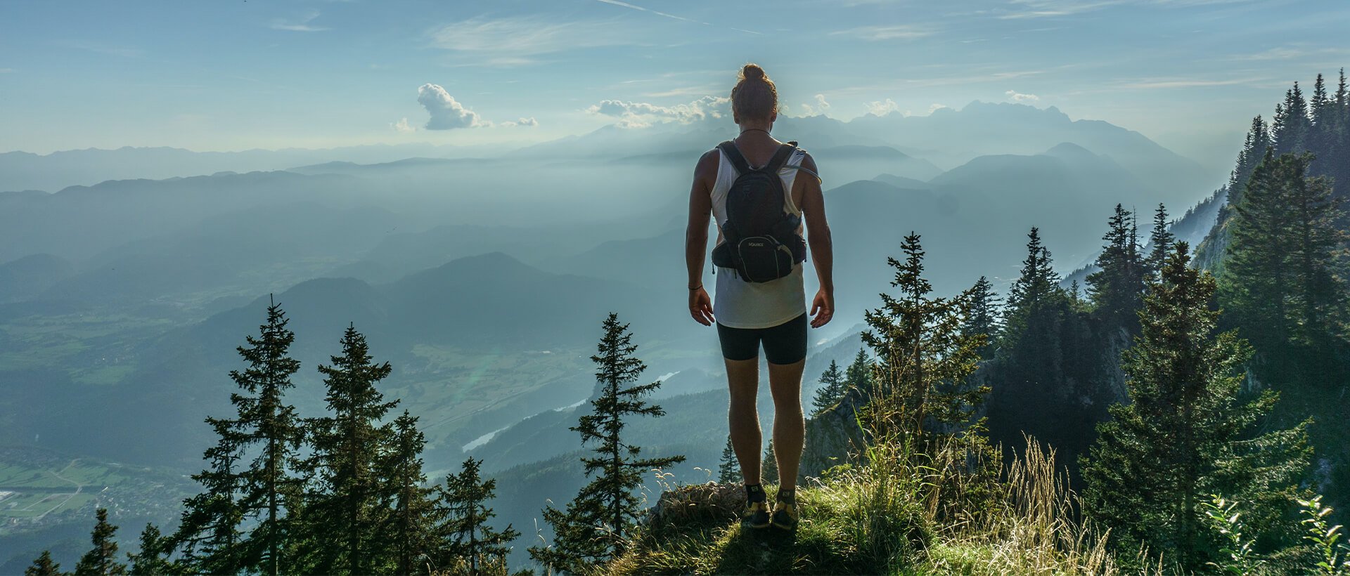 a woman standing on top of a lush green hillside.