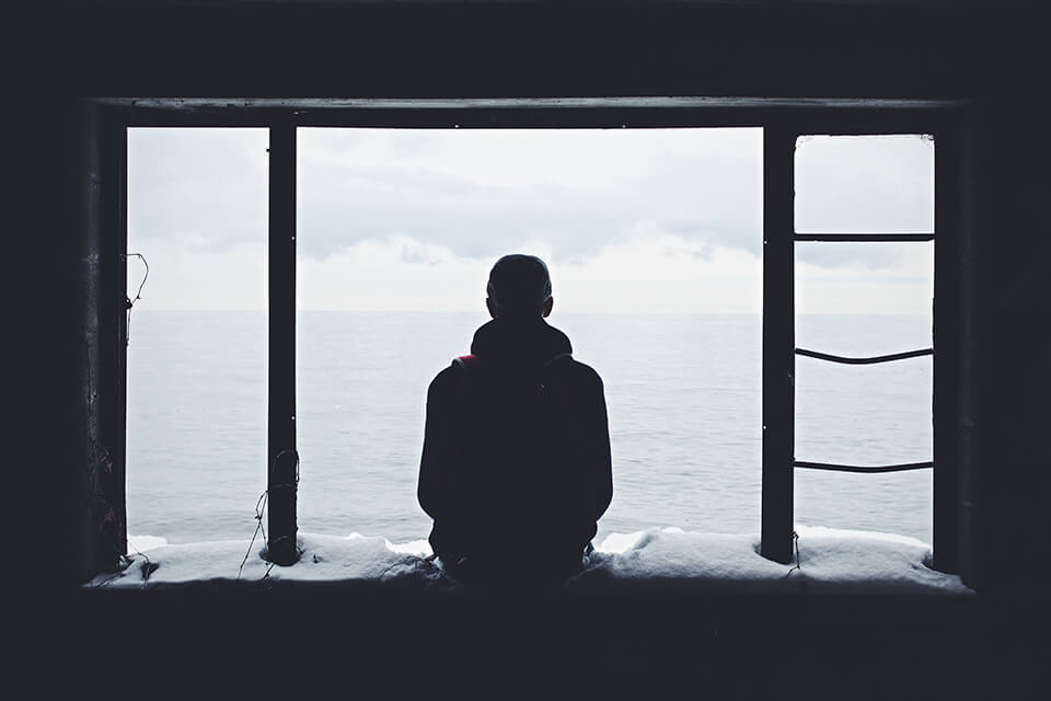 Man sitting on a window ledge looking at the water