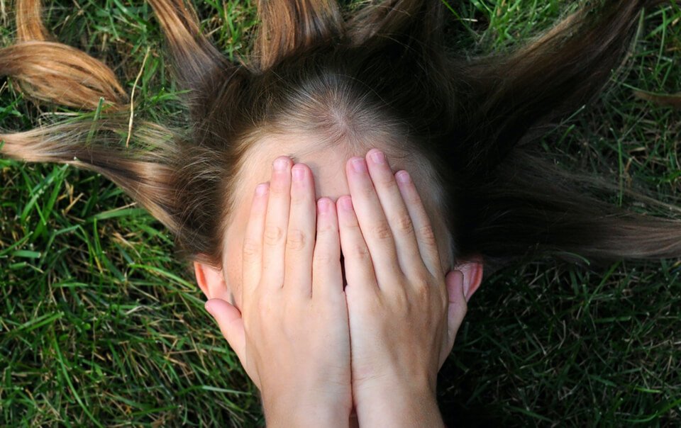 Woman covering face with hands and she's lays on the grass filled with anxiety