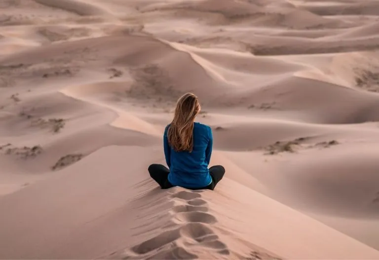 a woman sitting on top of a sand dune.