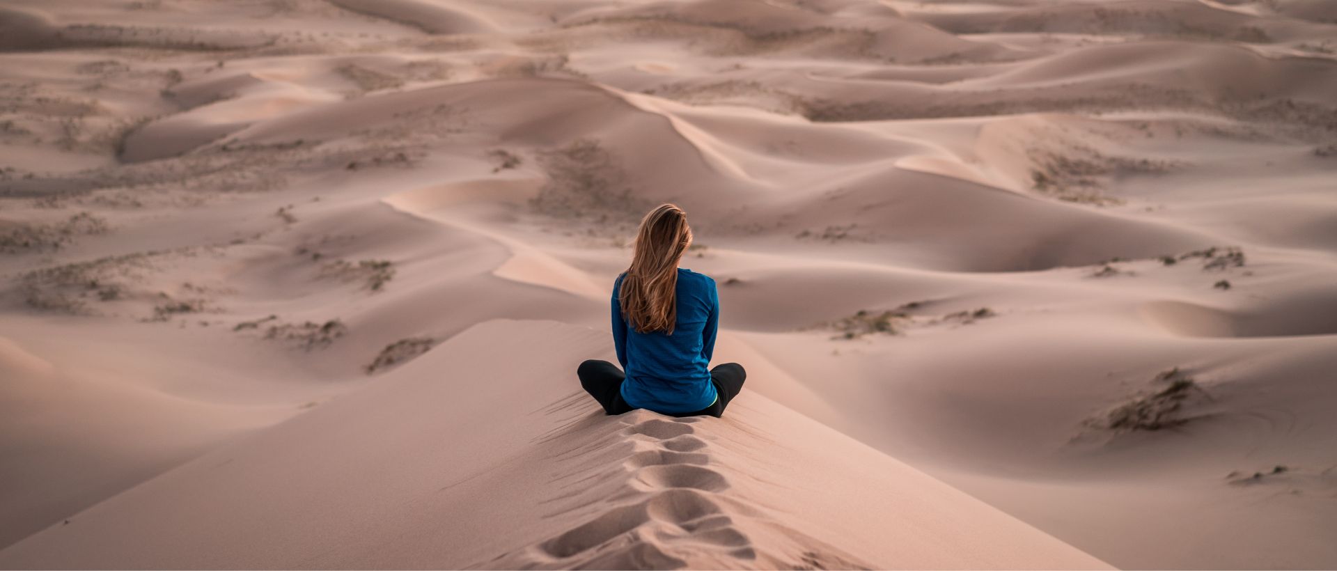 a woman sitting on top of a sand dune.