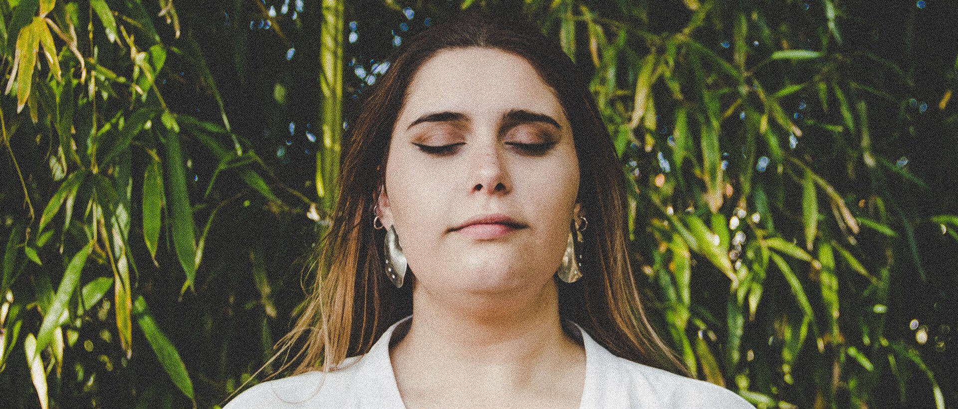 a woman with her eyes closed standing in front of a bamboo tree.