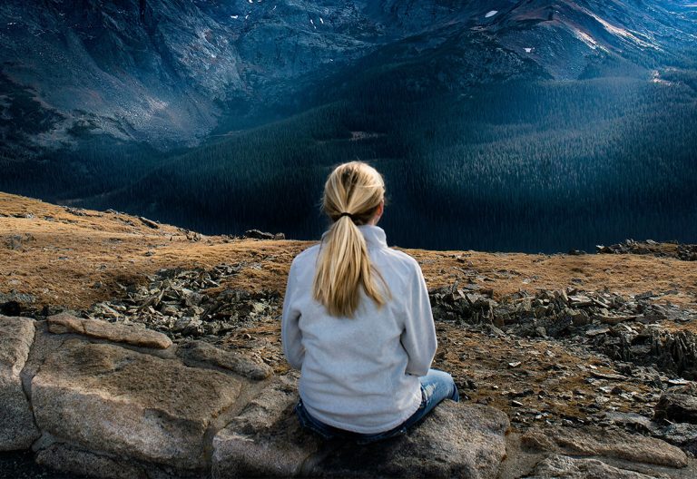 a woman sitting on top of a mountain overlooking a valley.