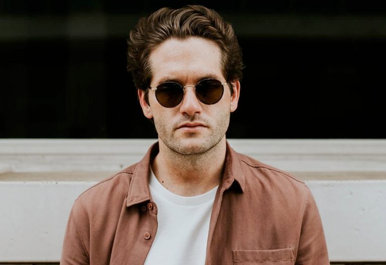 a man wearing sunglasses standing in front of a building.