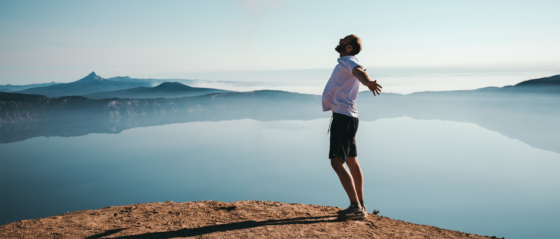 a man standing on top of a mountain next to a lake.