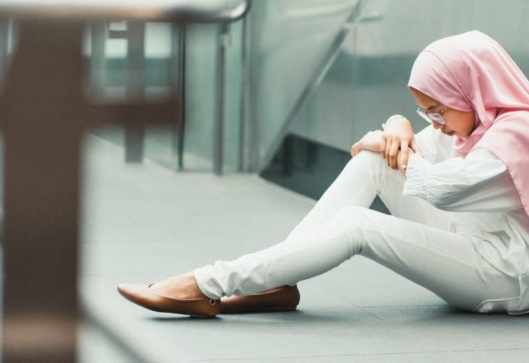 a woman sitting on the ground next to a wall.