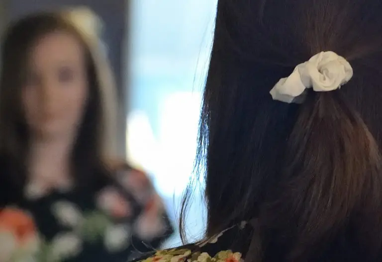 a woman standing in front of a mirror with a flower in her hair.