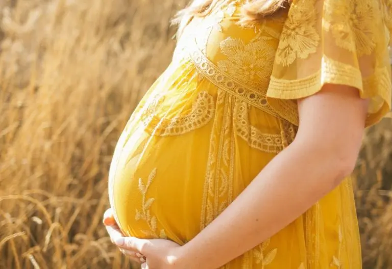 a pregnant woman in a yellow dress standing in a field.