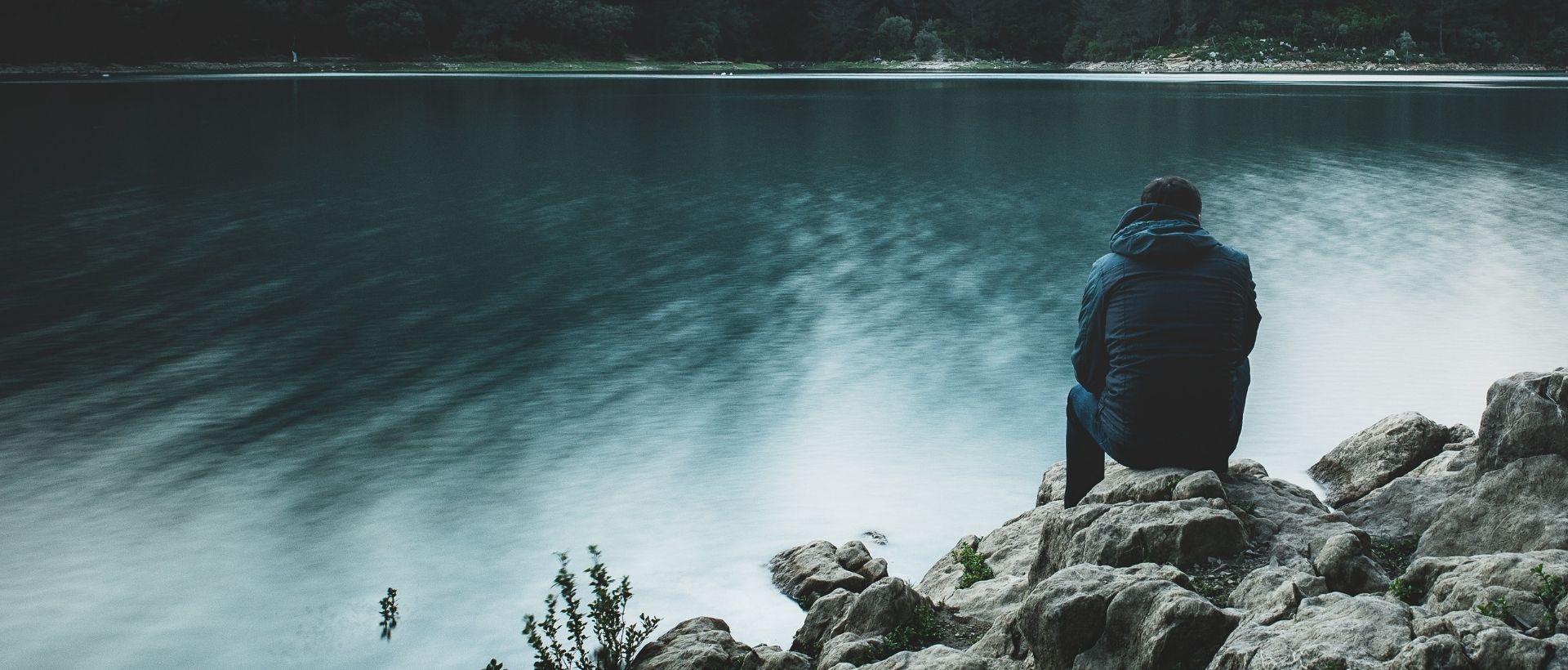 a person sitting on a rock looking at the water.