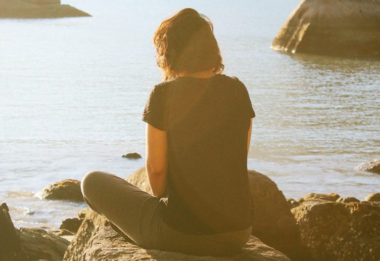 a person sitting on a rock looking out at the water.