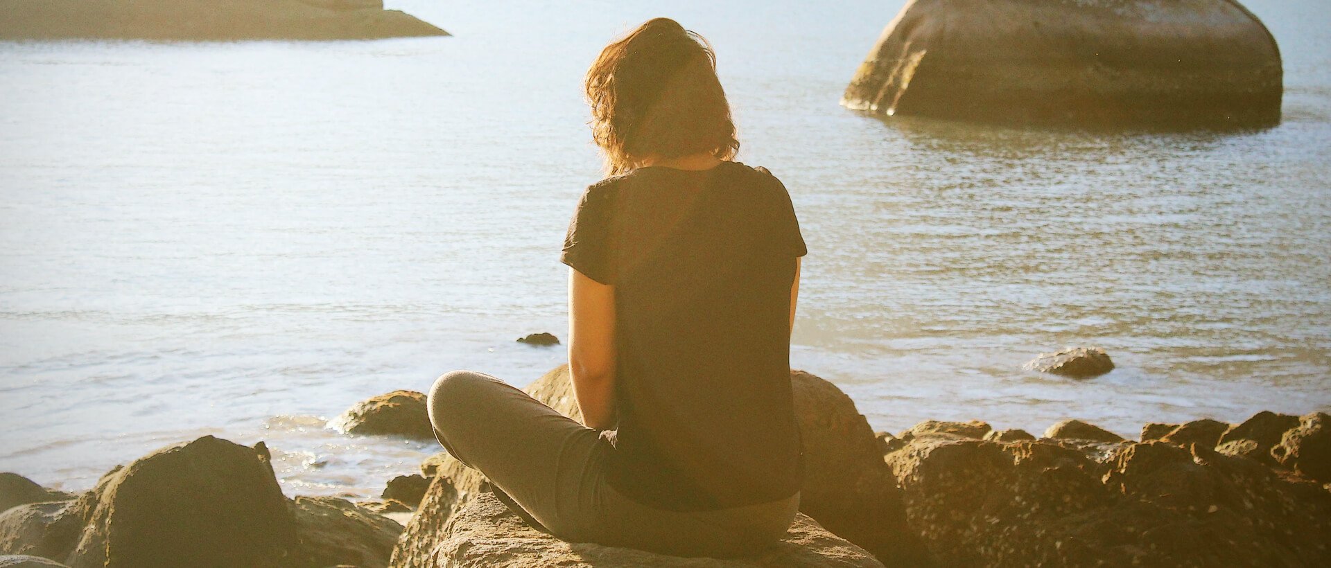 a person sitting on a rock looking out at the water.