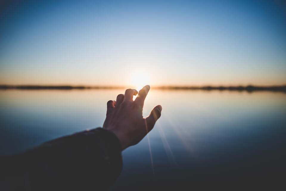 Hand reaching out to a sunset.