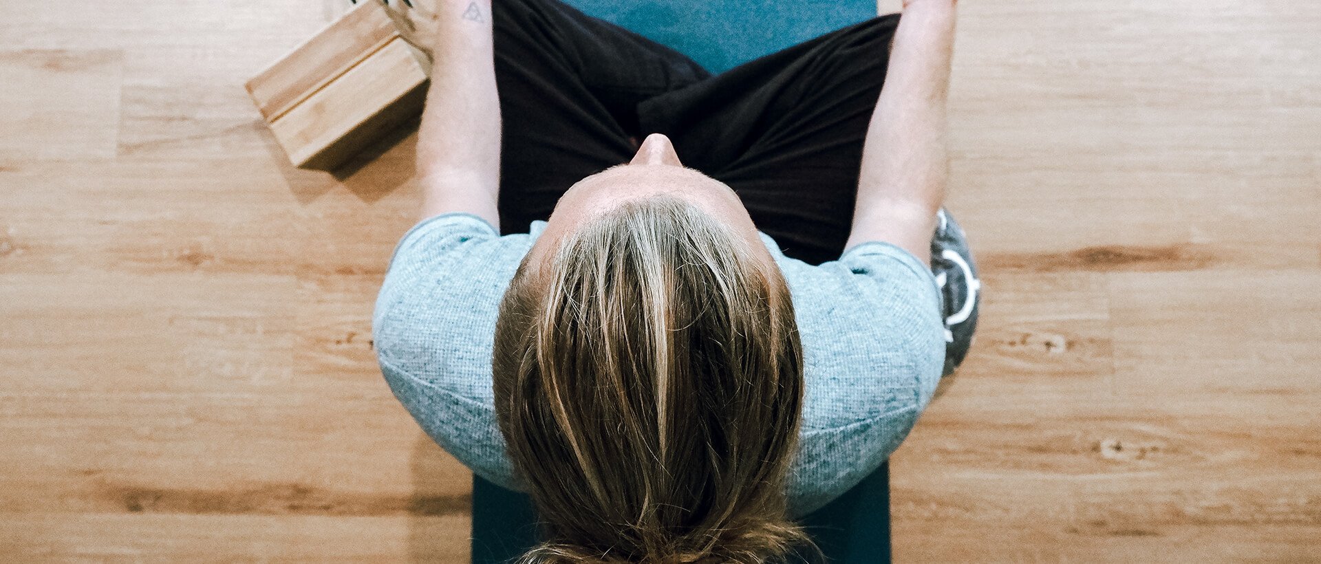 a woman sitting on a yoga mat with her hands behind her head.