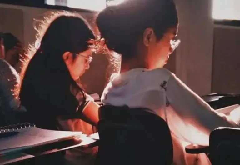 a couple of kids sitting at a desk in front of a laptop computer.