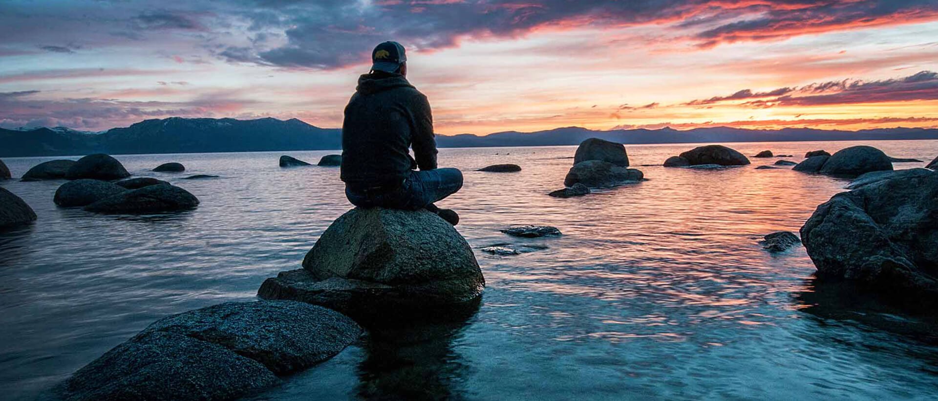 a person sitting on top of a rock near the ocean.