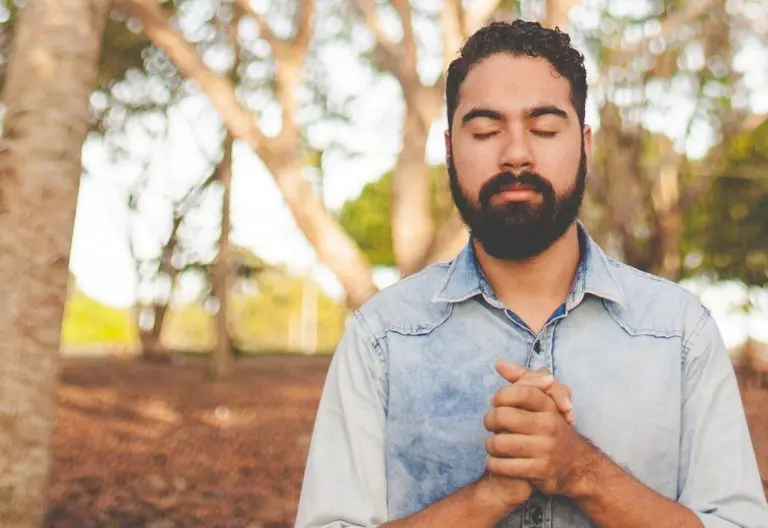 a man with a beard standing in front of trees.