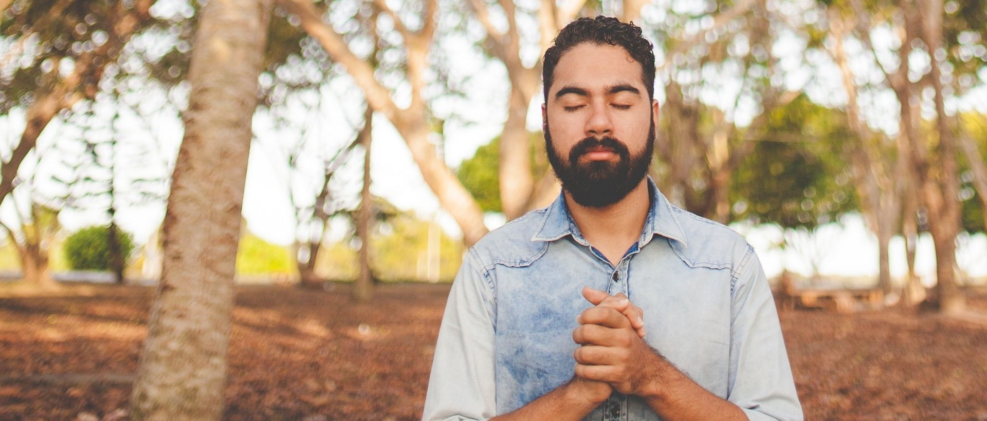 a man with a beard standing in front of trees.