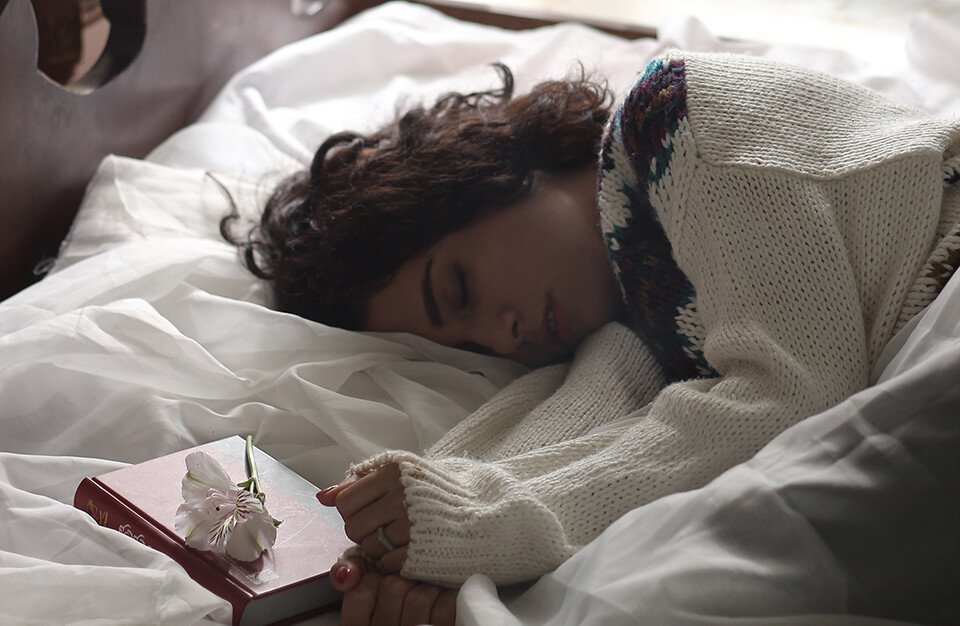 a woman laying in bed with a book and a flower.