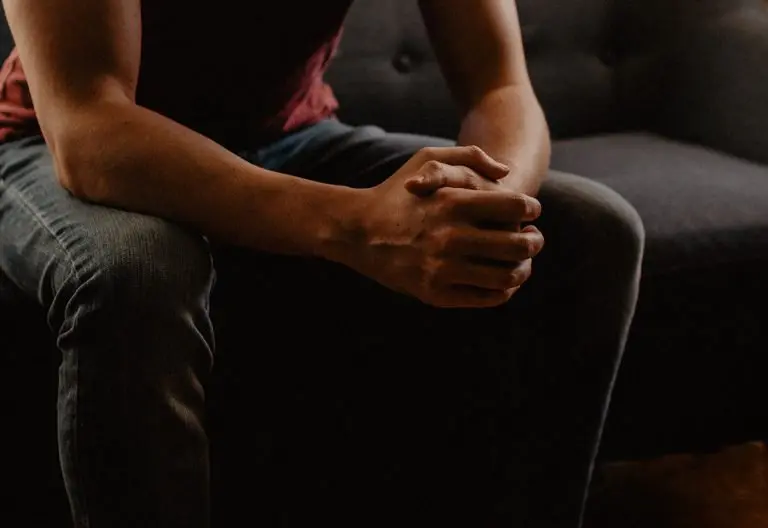 a person sitting on a couch with their hands clasped.