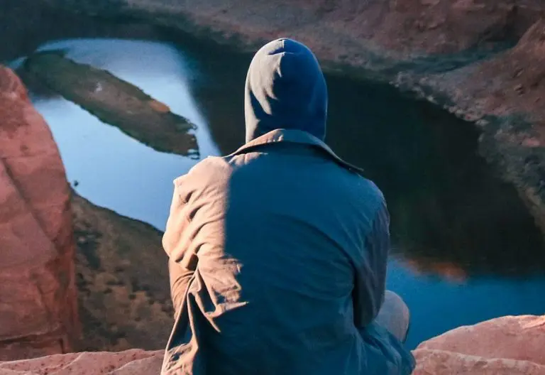 a person sitting on a rock looking at a lake.