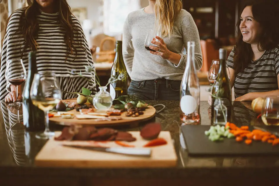 A group of women gathered around a kitchen table talking and drinking