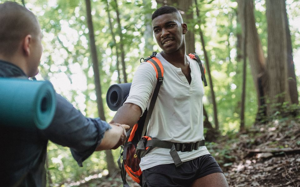 two men climbing uphill in a forest with yoga mats on their back