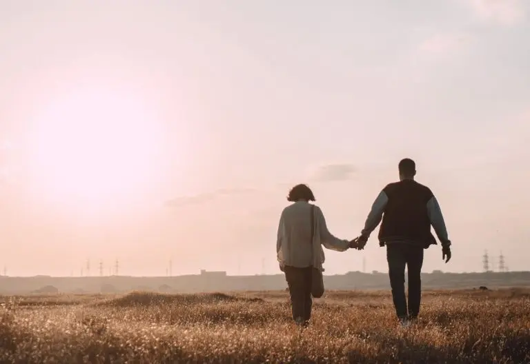 two people walking in a field holding hands.