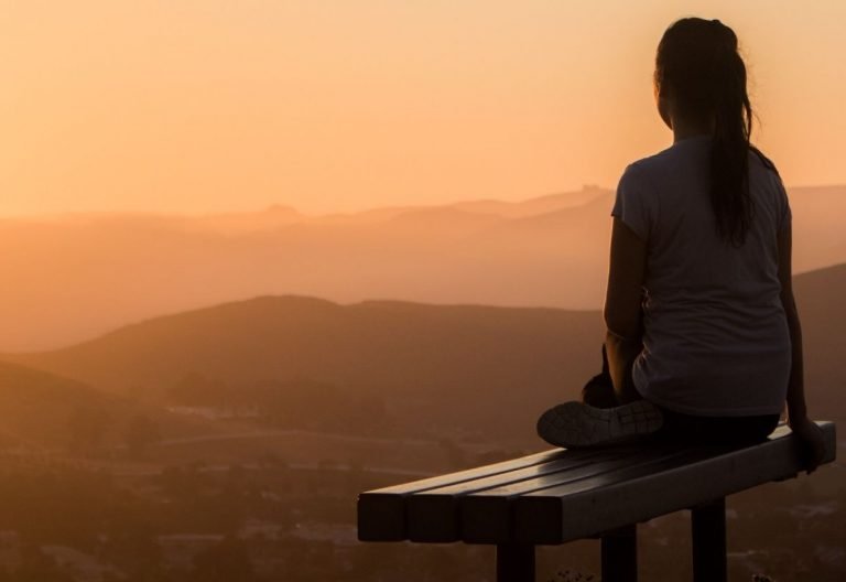 a woman sitting on a bench looking at the mountains.