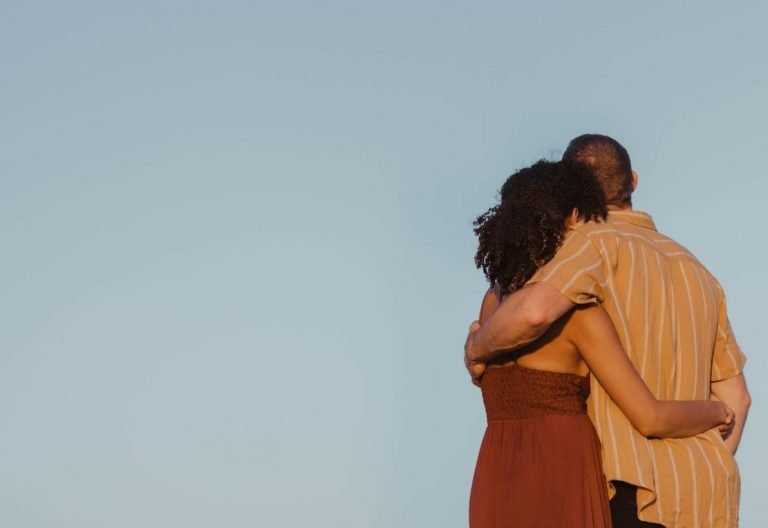 a man and a woman standing back to back with their arms around each other.