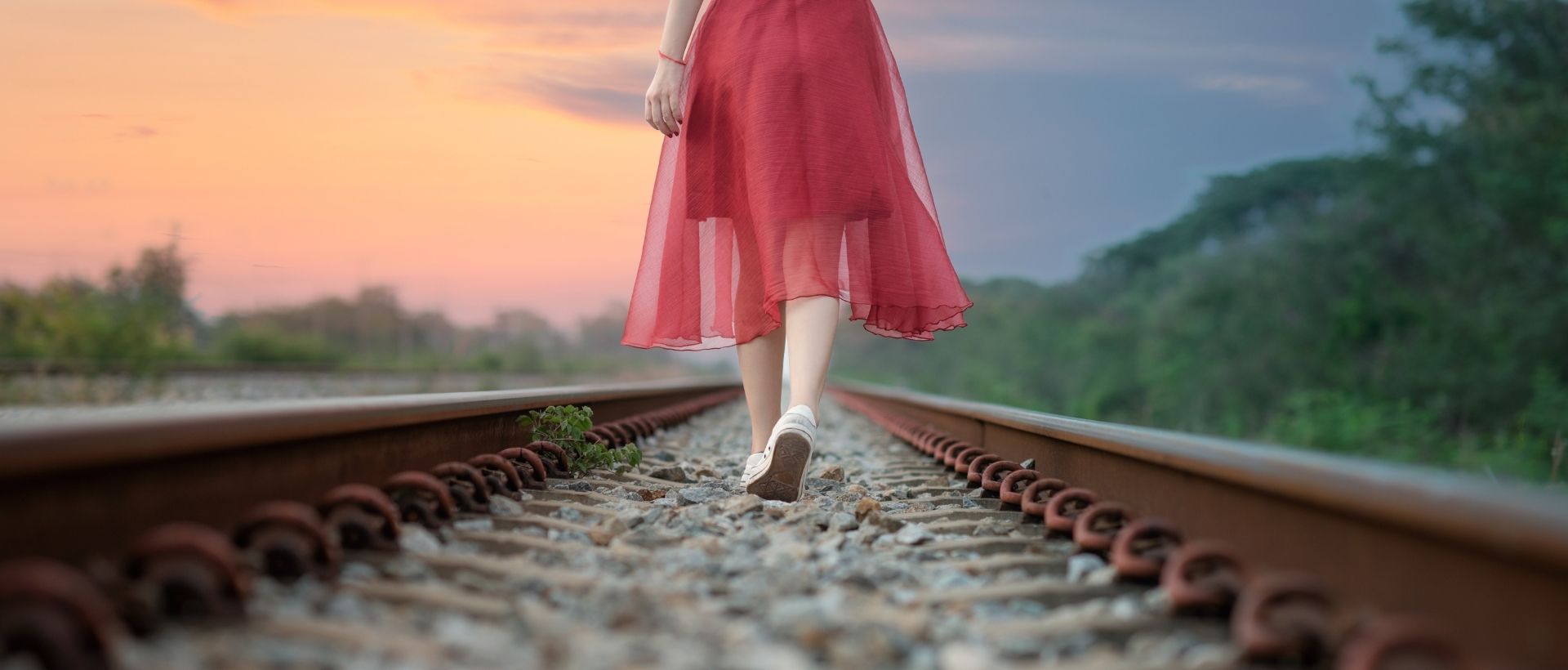 a woman in a red dress walking on a train track.