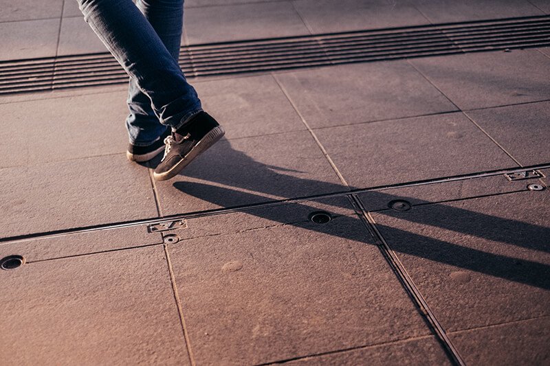 a person standing on a sidewalk with their shadow on the ground.