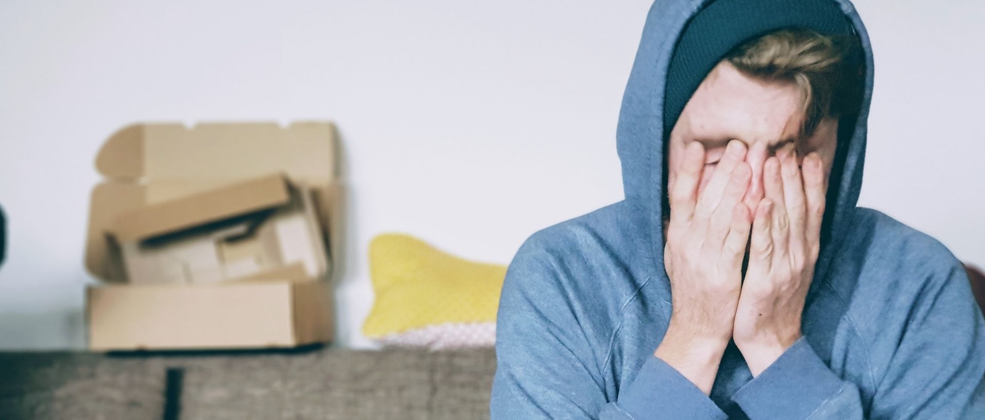 a man sitting on a couch covering his face with his hands.