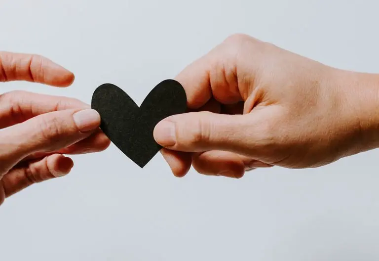 two hands holding a piece of paper in the shape of a heart.