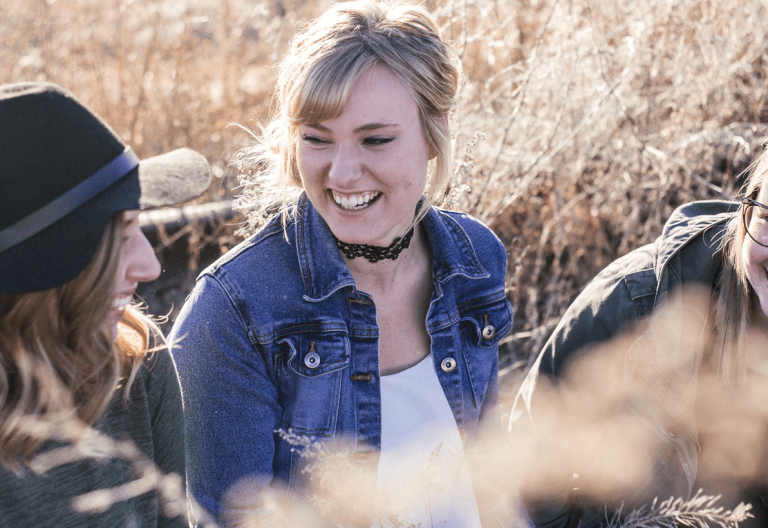 three young women laughing in a field of tall grass.