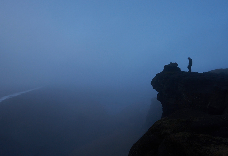 a person standing on top of a cliff on a foggy day.