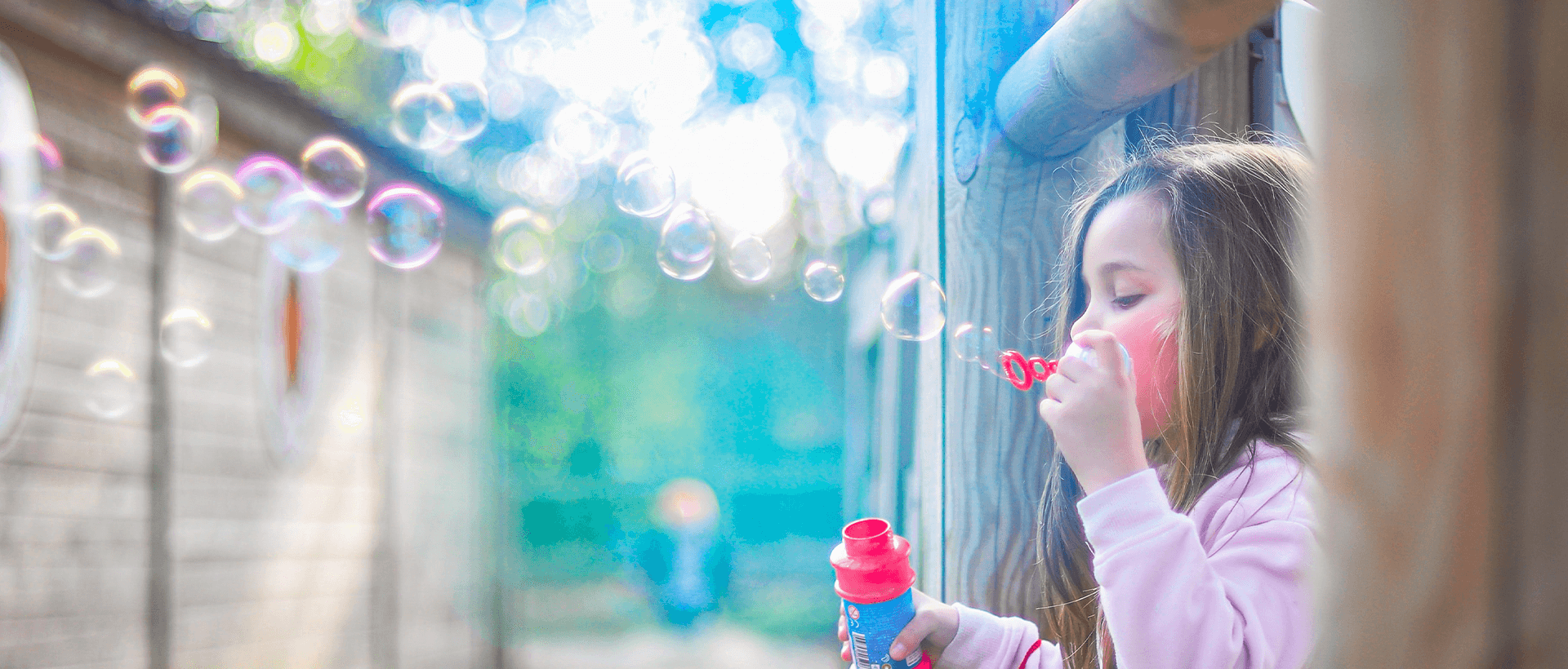 a little girl blowing bubbles out of a window.