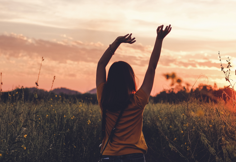 a woman standing in a field with her arms up.